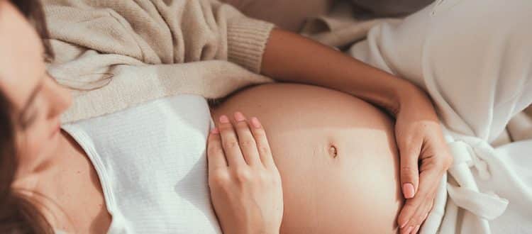 A pregnant woman cradling her exposed belly in her hands