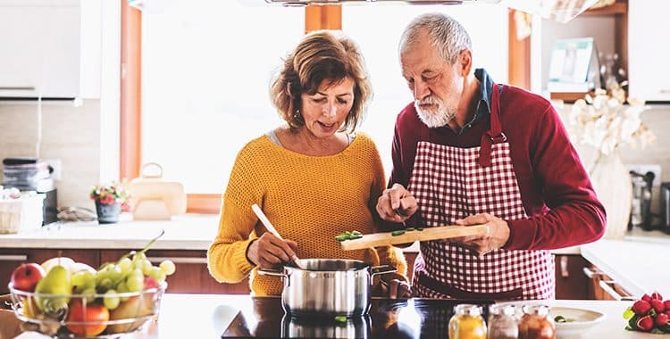 Elderly couple standing in the kitchen over a pot of food preparing a meal