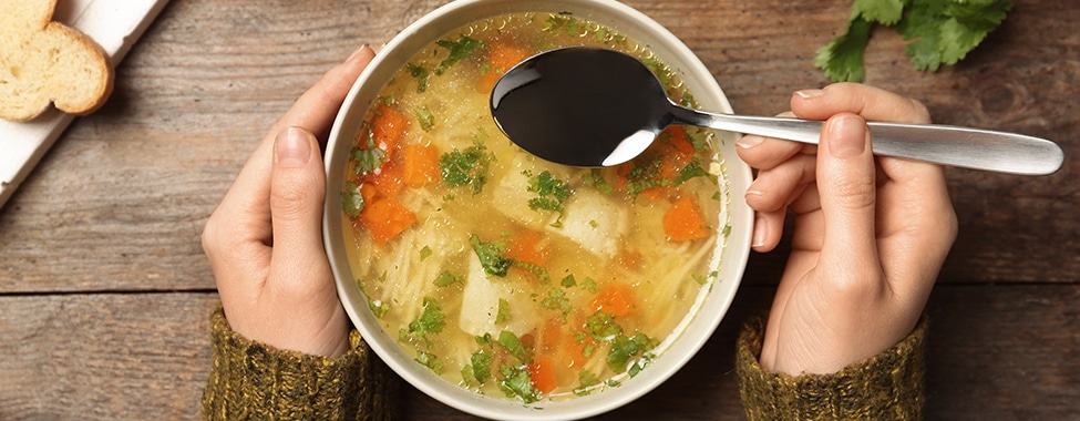 Person eating healthy chicken soup as a cold rememdy