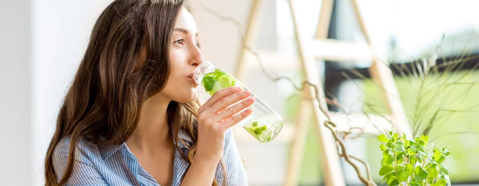 Woman drinking fruit-infused water from a glass bottle