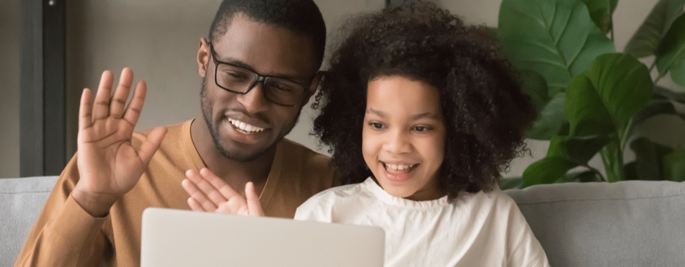 Father and daughter on a laptop video call, waving at the camera and smiling